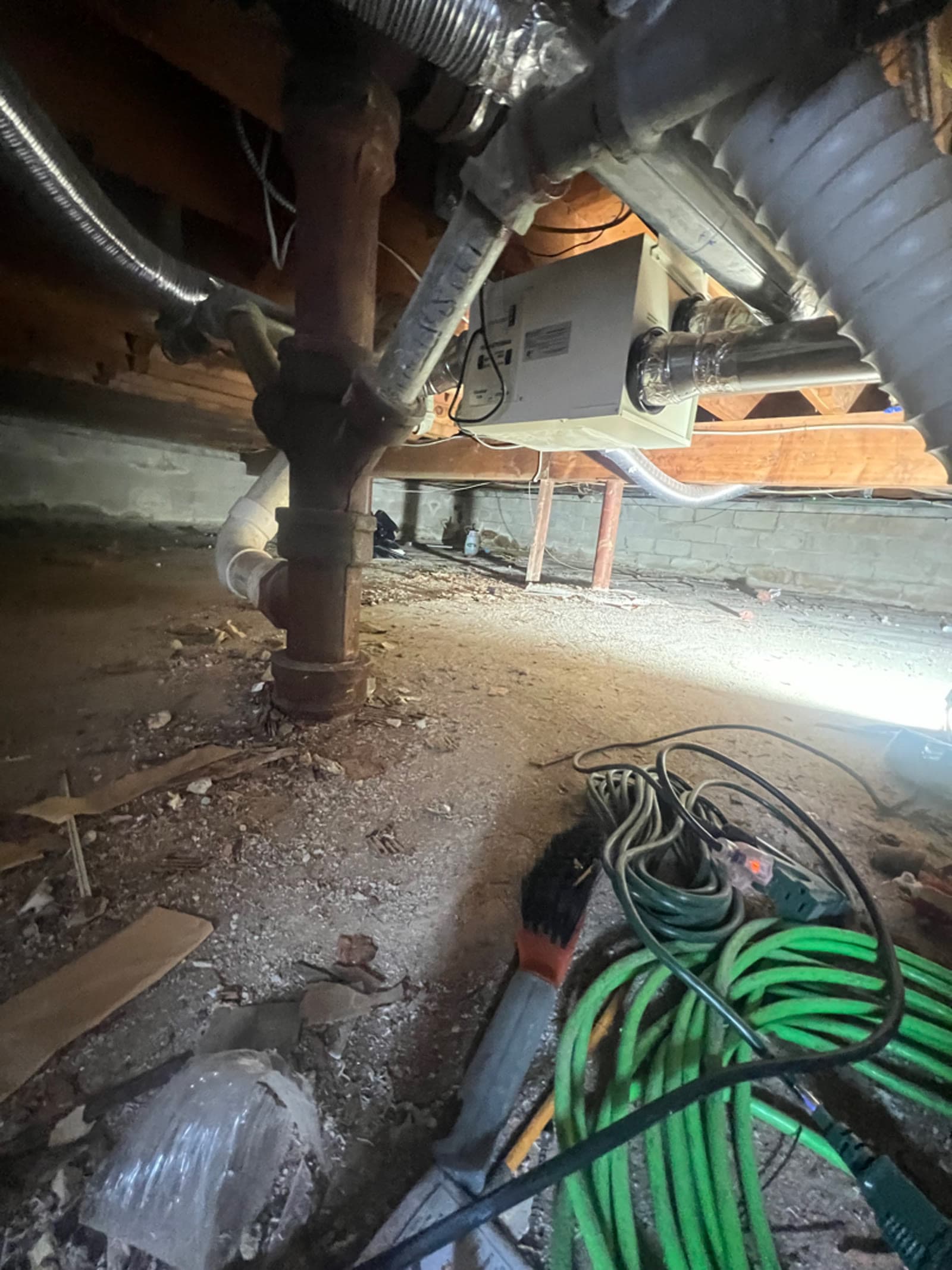 Crawl space under a Hartsdale, NY home with pipework, ductwork and debris across the floor before cleaning, before