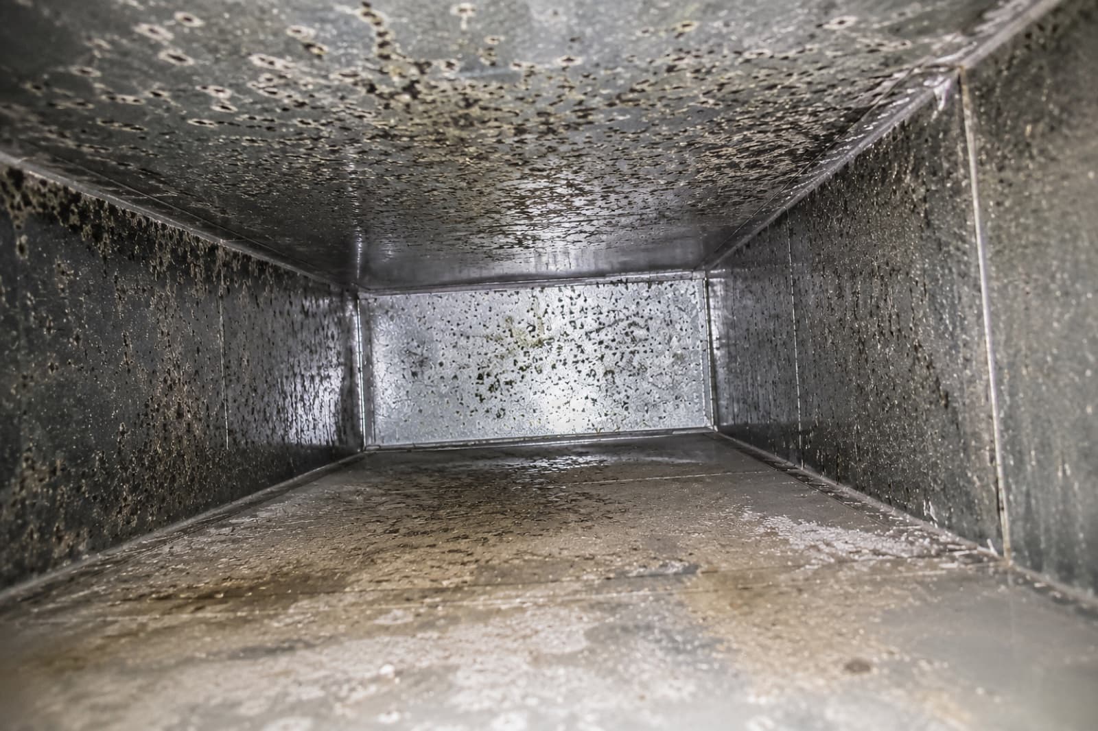 Residential HVAC air duct interior showing accumulated dust, debris, and particulate buildup on the galvanized sheet metal surface