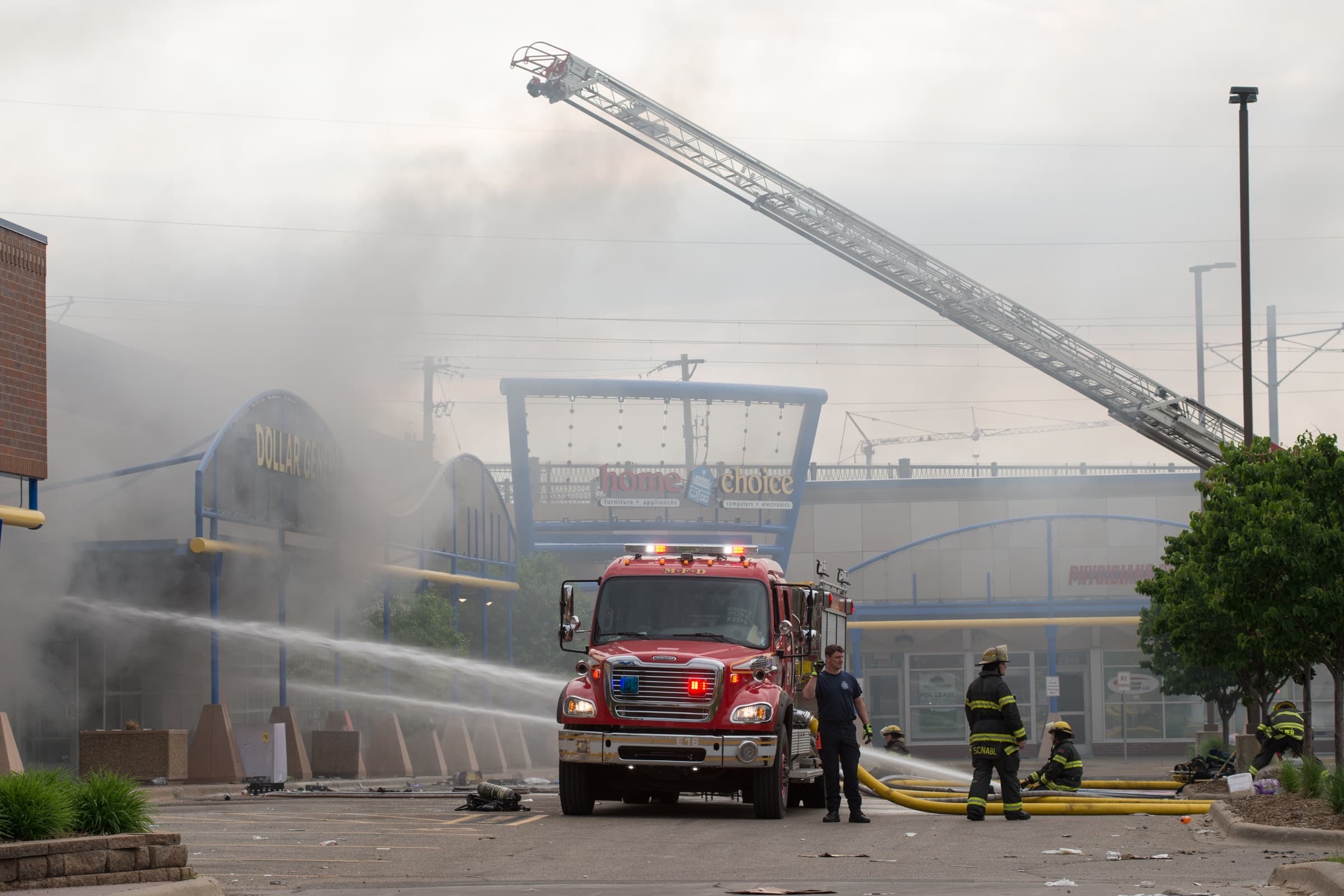 Firefighters with an aerial ladder battling fire and smoke at a multi-tenant commercial building