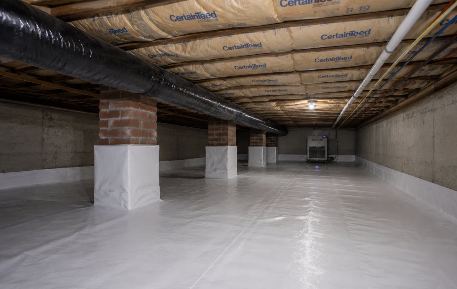 Fully encapsulated crawl space with white reinforced vapor barrier across the floor, wrapped brick support piers, R-19 batt insulation overhead, and a Santa Fe dehumidifier after a Green Restoration encapsulation in the tri-state