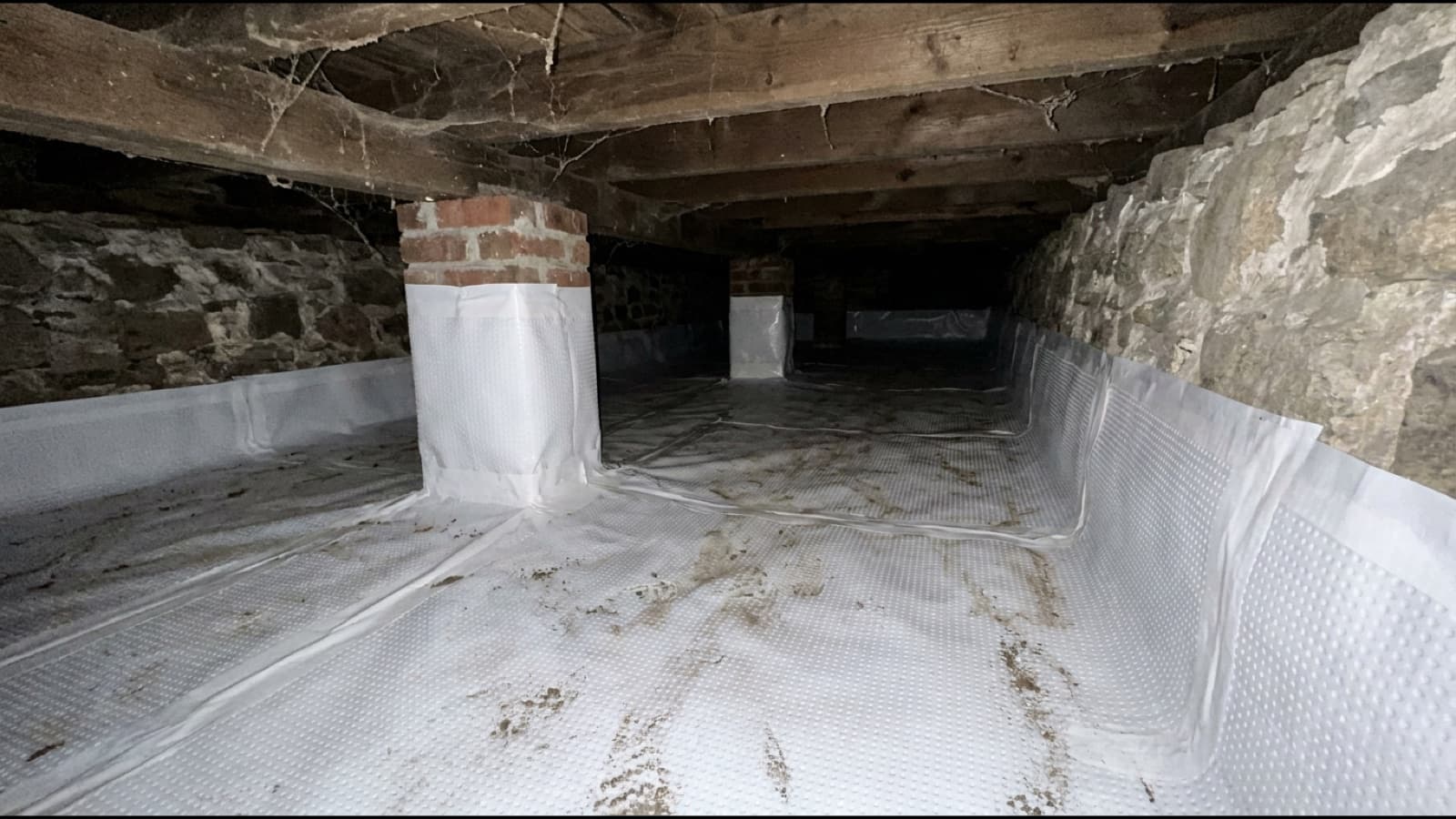 Encapsulated crawl space under a 1920s Connecticut home: white liner turned up the fieldstone wall with two wrapped brick piers