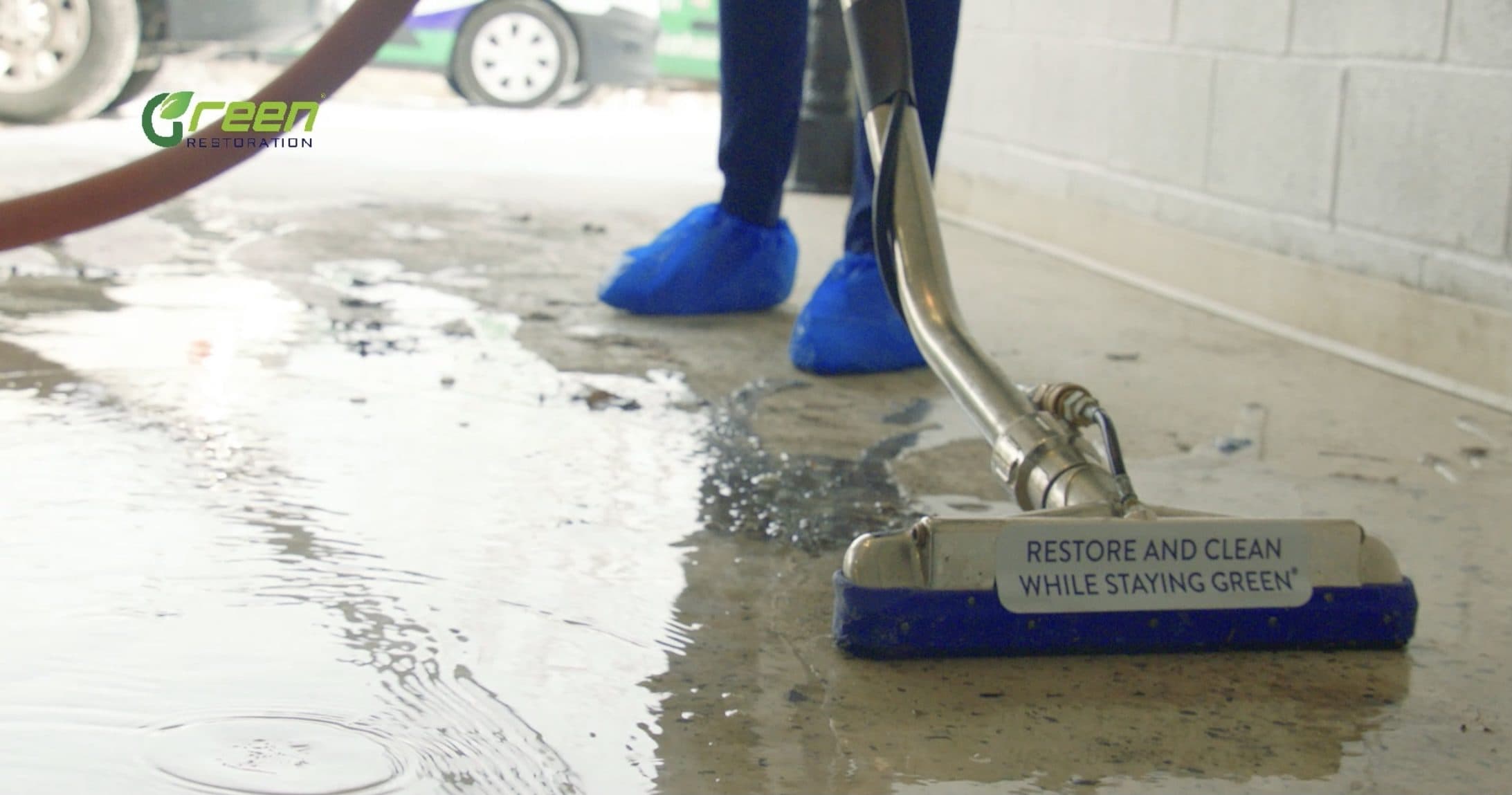 Green Restoration technician in protective shoe covers extracting standing water from a concrete floor with a stainless squeegee water-extraction wand