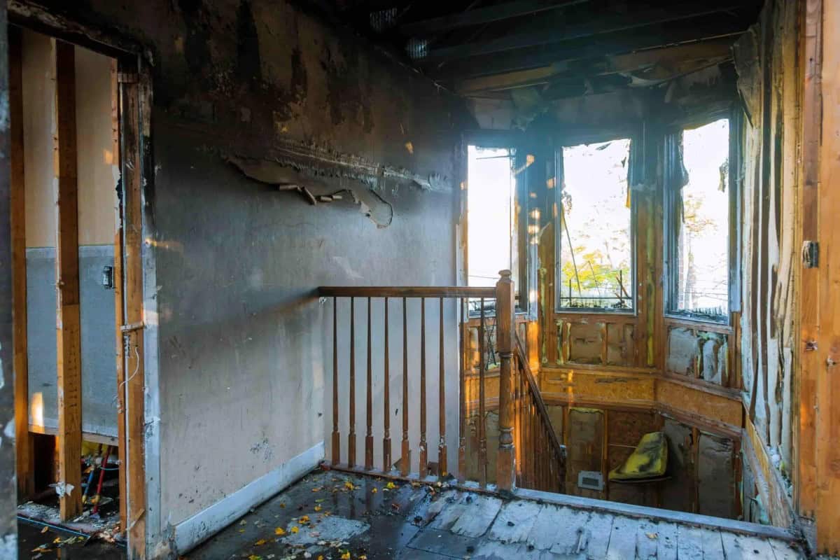 Exterior of a fire-damaged Colonial home with charred roof, smoke-stained siding, and emergency board-up plywood over windows, documented during a Green Restoration IICRC S700 fire damage scope assessment in Peekskill, Westchester County